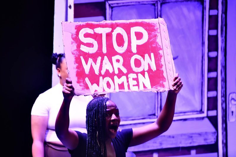 Woman during an anti-GBV protest, carries banner with words "Stop war on women".