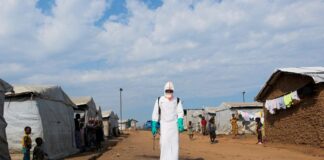 Health worker in PPE disinfecting an area during the burial of suspected Ebola victims at Kigonze displaced persons camp in Bunia, Democratic Republic of Congo.