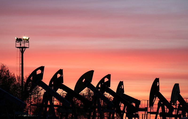 Pump jacks operate at the Airankol oil field under a sky with glowing sunset clouds.