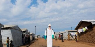Displaced people observe a health worker in full personal protective equipment disinfecting an area during the burial of suspected Ebola victims in a camp in eastern Democratic Republic of Congo.