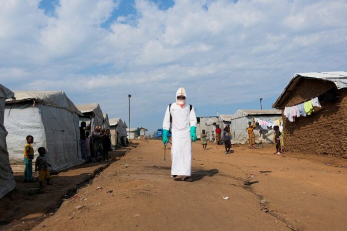 Displaced people observe a health worker in full personal protective equipment disinfecting an area during the burial of suspected Ebola victims in a camp in eastern Democratic Republic of Congo.