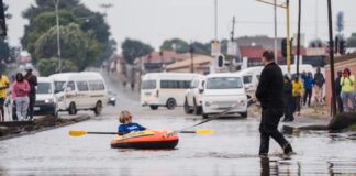 Helen Zille rowing a boat down a flooded street.