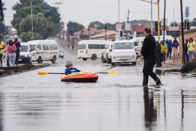 Helen Zille rowing a boat down a flooded street.