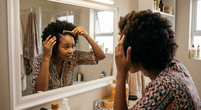 A Black South African woman with healthy afro-textured hair examining her scalp.