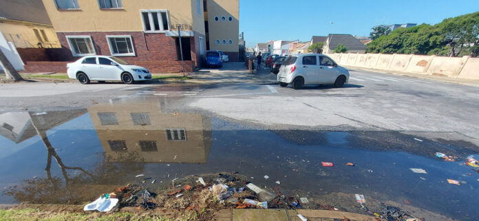Water leaking heavily from a damaged municipal pipe running down a road in eThekwini